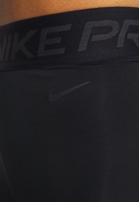 Detailní záběr na černý pas a tkaninu kompresních šortek Nike Pro, na kterých je viditelné jemné logo značky Nike.