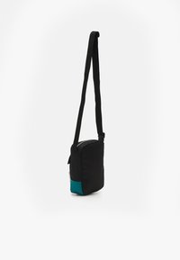 Svart tyg crossbody-väska med en teal-färgad botten. Har en dragkedja i toppen och justerbar axelrem. Kompakt rektangulär design.