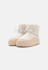 Bottines en polaire blanche avec une texture douce, bout rond et semelle en caoutchouc beige contrastante ; dotées de lacets blancs et d'un petit accent doré.