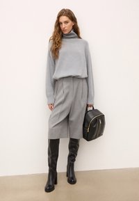 Svetlo sivi pleteni turtleneck pulover, sivi plisirani culottes, črne škornje do kolen, drži črn nahrbtnik z zadrgo.