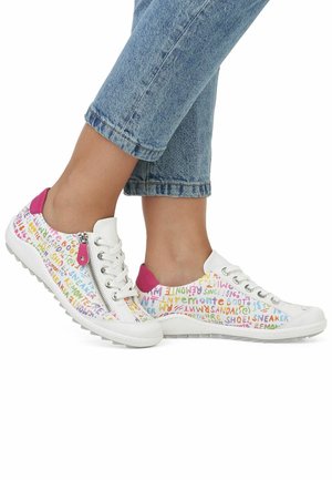 Zapatillas blancas con patrones de texto coloridos, detalles en el talón rosa y cremallera lateral. Suela de goma, diseño bajo, combinadas con jeans azules arremangados.