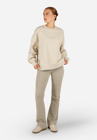 Šviesiai ruda per didelė megzta palaidinė su grioveliais ant rankovių ir apačios, derinama su šviesiai pilkomis grioveliais megztomis pašlyjančiomis kelnėmis. Modelis vilki šviesiai rudus batus.