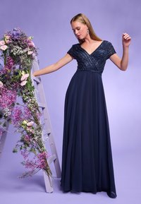 Robe longue bleu marine avec un corsage en V ornée de perles et des manches courtes. Jupe en chiffon fluide qui descend jusqu'au sol. Accents floraux à proximité.