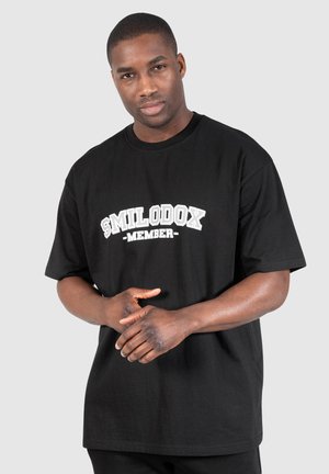 Schwarzes Baumwoll-T-Shirt mit lockerer Passform, mit weißem "SMILODOX MEMBER"-Text in einem fetten, gewölbten Design über der Brust.