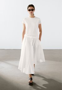 Hvid bomulds T-shirt parret med en flydende hvid nederdel og sorte platform-sandaler. Nederdelen har en elastisk talje og sidelommer.