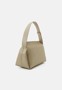 Borsa a tracolla in morbida pelle beige con forma trapezoidale strutturata e una larga tracolla singola regolabile.