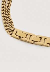 Zlatý kovový náramok s prepojenými očkami, ktorý obsahuje kombináciu plochých a zaoblených častí, s lešteným povrchom a bezpečnou sponou.