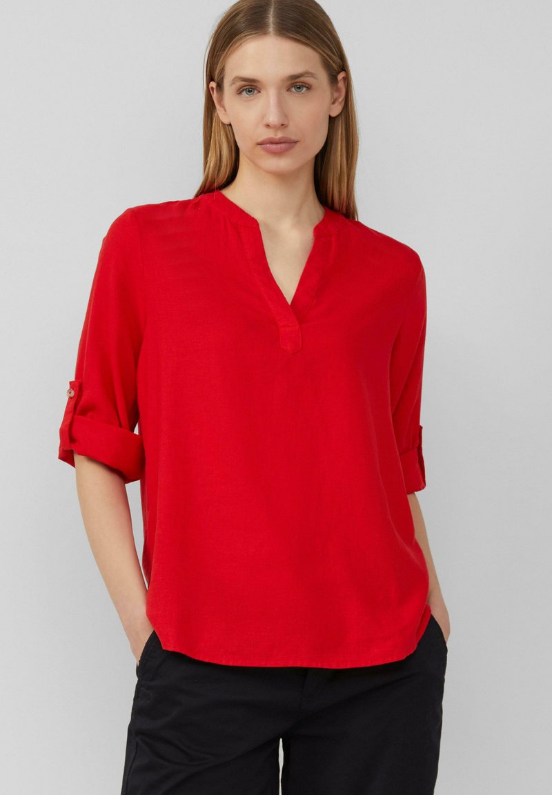 Blouse rouge à manches longues avec un décolleté en V et des poignets retroussés, fabriquée en tissu léger, présentant une coupe décontractée et une texture lisse.