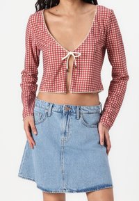 Rot-weißer kariertes Langarm-Crop-Top mit V-Ausschnitt und Bindeband, kombiniert mit einem hellblauen Jeans-A-Linien-Rock.