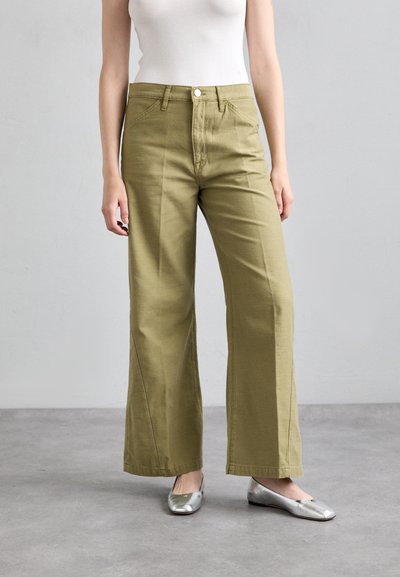 Pantaloni ampi di colore verde oliva realizzati in un tessuto misto cotone. Presentano una chiusura con bottone, passanti per la cintura e tasche laterali. Ballerine piatte argentate.
