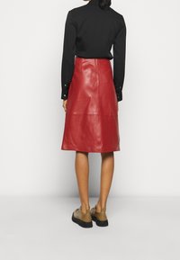 Falda midi de cuero rojo con corte recto, textura suave y cintura alta. Combinada con una blusa negra de manga larga y zapatos beige.