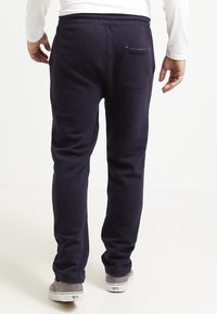 Marinblå joggingbyxor med slim fit, elastisk midjeband och bakficka. Tillverkade av mjukt, texturerat tyg, i kombination med grå skor.