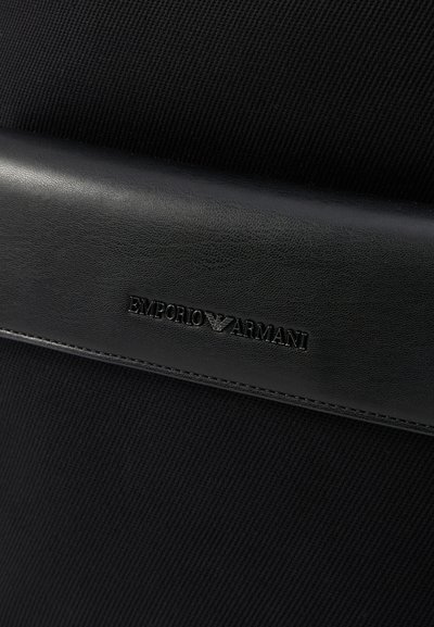 Fekete szövet táska struktúrált felülettel. Sima fekete bőrből készült díszítéssel és domborított "Emporio Armani" logóval rendelkezik. Egyszerű dizájn, téglalap alakú.