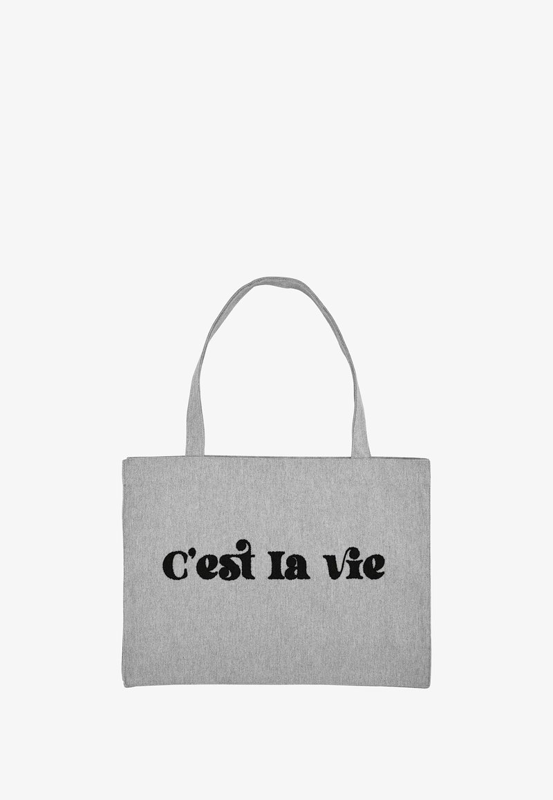 Pilka audinio pirkinių rankinė su dviem rankenomis, priekyje užrašyta „C’est la vie“ ryškiomis juodomis raidėmis.