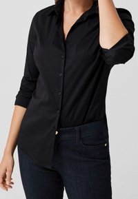 Schwarze Langarm-Bluse mit klassischem Kragen, glatter Textur und hochgerollten Ärmeln, kombiniert mit dunklen Jeans.