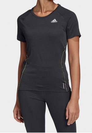 Persona vistiendo una camiseta atlética de manga corta negra de Adidas y mallas negras a juego, de pie con los brazos relajados a los lados.