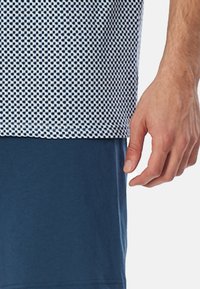 Navy blue short-sleeve shirt with a white geometric pattern at the top. Smooth texture, relaxed fit, and contrasting design elements.