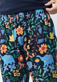 Dunkelblaue Hose mit bunten Blumen- und blauen Elefantenmustern, elastischem Bund mit Kordelzug und einer Hand, die die Taille anpasst.