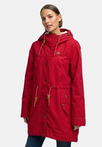 Cappotto impermeabile rosso con cappuccio, vita regolabile con drawstring e bottoni a pressione. Presenta tasche laterali e dettagli in metallo color oro.