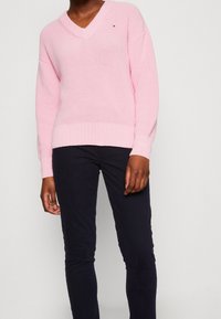 Maglione lavorato a maglia di un rosa chiaro con scollo a V, caratterizzato da un taglio ampio e una texture a coste. Abbinato a pantaloni slim-fit di un blu navy scuro.