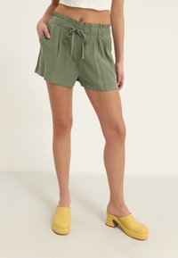 Groene, lichtgewicht stoffen korte broek met een ontspannen pasvorm, elastische tailleband en trekkoord. Gecombineerd met gele plateausabots.