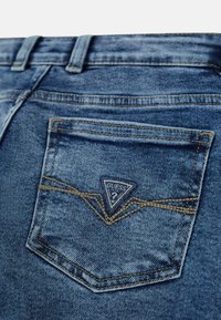 Jeans in denim con un lavaggio azzurro chiaro, caratterizzati da un patch triangolare con il logo Guess sulla tasca posteriore e dettagli di cucitura a contrasto.
