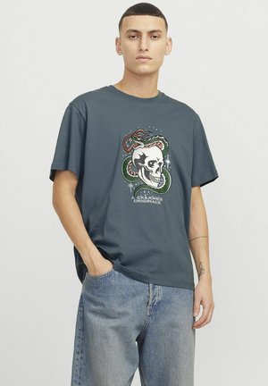 Tamno plava pamučna majica koja prikazuje grafiku lubanje okružene zmijom. Dizajn uključuje zvijezde i tekst "Jack & Jones Originals."
