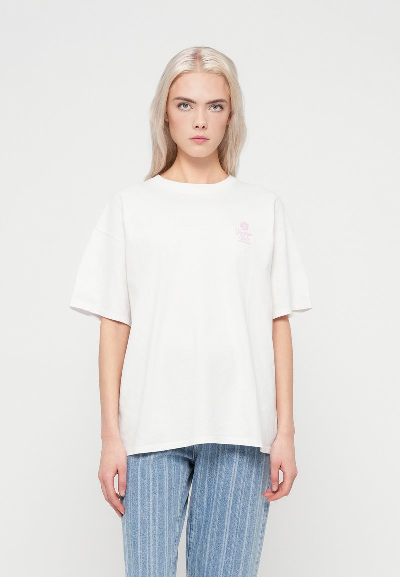 Hvid bomulds t-shirt med korte ærmer, rund hals og et lille pink blomstermotiv på venstre bryst. Båret med lyseblå stribede jeans.