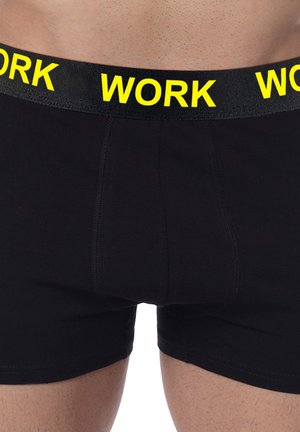 Schwarze Boxershorts mit glatter Textur, ausgestattet mit einem breiten schwarzen Bund, der mit auffälliger gelber "WORK"-Schrift bedruckt ist.