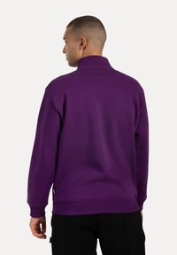 Sudadera púrpura con un cuello alto, puños y dobladillo acanalados; textura suave y corte relajado. Vista trasera de la prenda mostrada.