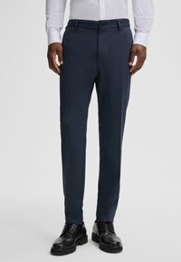 Granatowe, dopasowane spodnie wykonane z teksturowanej tkaniny, z zamkiem błyskawicznym, szlufkami na pasek i smukłym krojem, w połączeniu z czarnymi butami.