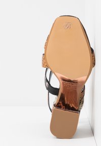 Sandale à talons hauts noire et beige en cuir imprimé serpent, avec des lanières fines et une semelle lisse de couleur claire.