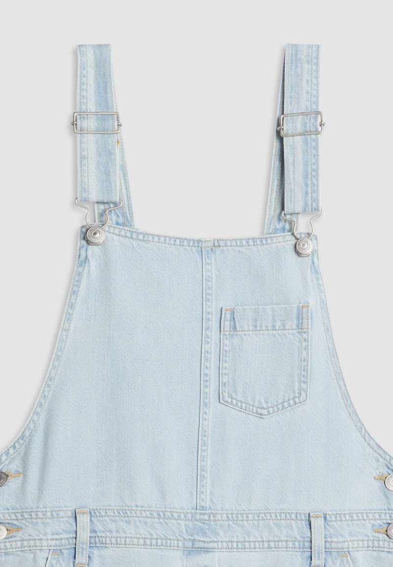 Hellblaue Jeanslatzhosen mit verstellbarem silbernem Zubehör, einer kleinen Vordertasche und Nahtdetails an den Nähten.