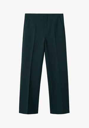 Femme portant un trench beige sur un pull col roulé court blanc, un pantalon large taille haute vert foncé et des talons blocs noirs.