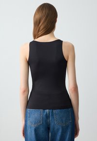 Top nero senza maniche con scollatura rotonda, realizzato in un tessuto morbido. Abbinato a jeans in denim azzurro chiaro a vita alta con tasche posteriori.