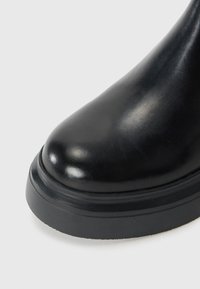 Black leather ankle boot with a rounded toe, smooth texture, and a contrast rubber sole. Features a subtle shine and no visible hardware.