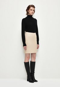 Svart rullkragetröja, ljusbeige figurnära kjol och svarta knähöga klackstövlar. Släta texturer och enkel design. Minimalistisk estetik.