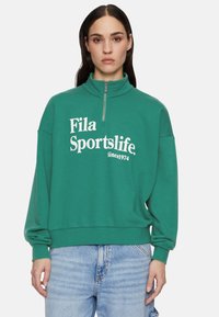 Felpa verde in pile con colletto alto e mezza zip, con testo bianco "Fila Sportslife" e una vestibilità cropped. Polsini e orlo a coste.