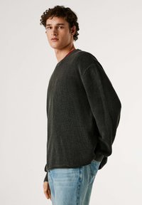 Sweat-shirt gris foncé texturé à manches longues avec un col rond, doté d'un accent rouge sur l'encolure. Associé à un jean bleu clair.