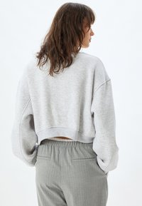 Sudadera corta gris con una textura suave, mangas de gran tamaño y dobladillo acanalado, combinada con pantalones de rayas grises claros.