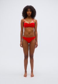 Κόκκινο σετ μαγιό με τοπ τύπου bandeau και ταιριαστό μαγιό με χαμηλή μέση. Λείο ύφασμα, μίνιμαλ σχεδιασμός, χωρίς ορατά μεταλλικά στοιχεία.