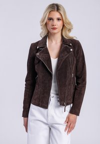 Giacca da motociclista in suede marrone con cerniere e bottoni a pressione argentati. Presenta un davanti asimmetrico e una silhouette aderente.