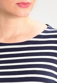 Pruhované tričko v námořnické modři a bílé barvě s kulatým výstřihem. Tkanina vypadá měkce a pleteně, ukazuje hladkou strukturu a rovnoměrné švy.