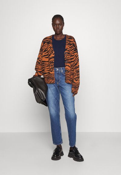 Orange and black striped cardigan, navy top, loose blue jeans, and black shoes. Model holds a black leather bag.