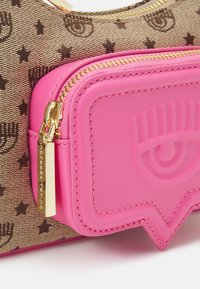 Hnědá vzorovaná kabelka s kováním ve zlaté barvě, vybavená jasně růžovou koženou kapsou s texturovaným designem a zlatým zipem.