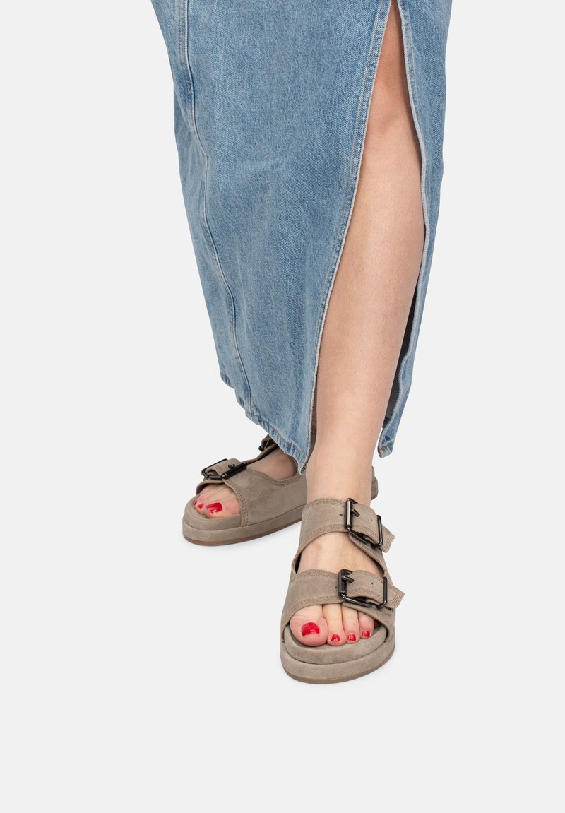 Sandali beige con due fibbie regolabili, texture in suede, design con punta aperta, abbinati a una gonna maxi in denim con uno spacco laterale.