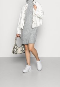 Robe en maille grise avec ourlet côtelé, veste bomber blanche courte, sac à main à motif serpent, et baskets blanches à semelles épaisses.