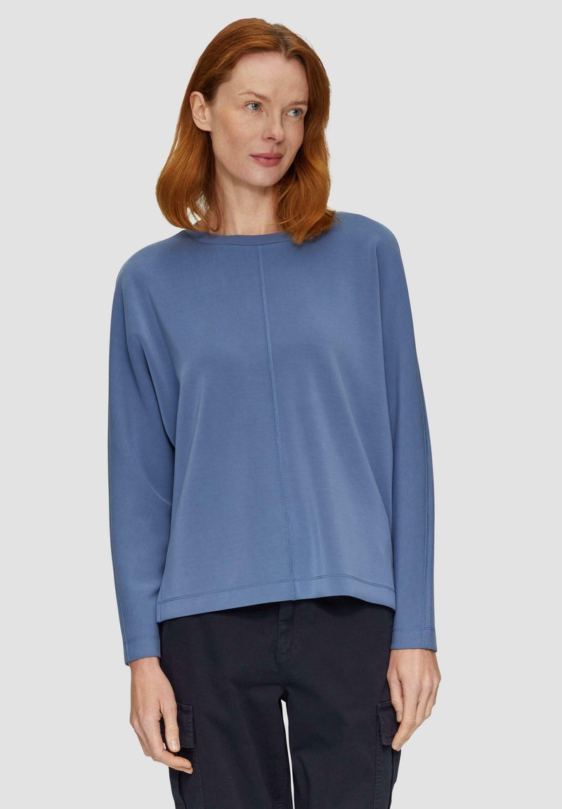 Blaues Sweatshirt mit langen Ärmeln, Rundhalsausschnitt und sichtbaren Nahtdetails. Der Stoff hat eine glatte Textur. Getragen mit dunklen Cargo-Hosen.