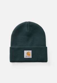 Mørkegrønn ribbestrikket lue med brettet oppkant som har en firkantet hvit lapp og oransje Carhartt-logo.