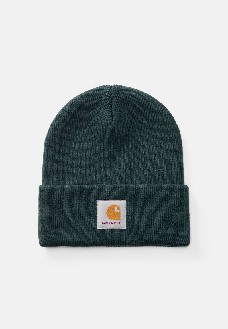 Mørkegrønn ribbestrikket lue med brettet oppkant som har en firkantet hvit lapp og oransje Carhartt-logo.